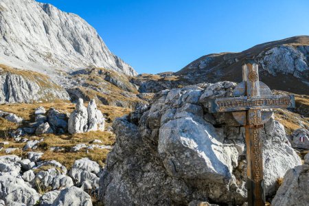 Photo for Small, wooden cross on top of a passage in the region of Hochschwab in Austrian Alps. There are massive stony wall in the back. The flora overgrowing the slopes is golden. Spirituality, memory place - Royalty Free Image