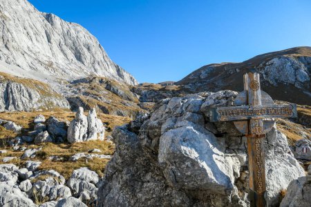 Photo for Small, wooden cross on top of a passage in the region of Hochschwab in Austrian Alps. There are massive stony wall in the back. The flora overgrowing the slopes is golden. Spirituality, memory place - Royalty Free Image