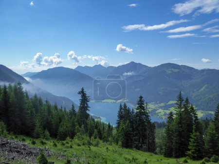Téléchargez les photos : An idyllic view from the side of the mountain on a distant Weissensee lake in Austria. The lake is surrounded by high Alps. Few clouds above the peaks. High mountains around. Calmness - en image libre de droit