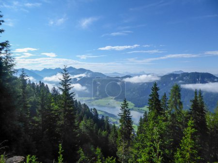 Téléchargez les photos : An idyllic view from the side of the mountain on a distant Weissensee lake in Austria. The lake is surrounded by high Alps. Few clouds above the peaks. High mountains around. Calmness - en image libre de droit