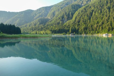 Téléchargez les photos : A shore line of Weissensee lake in Austrian Alps. The water has strong turquoise color. Green shore of the lake. A small village at the side of the lake. Serenity and peacefulness - en image libre de droit