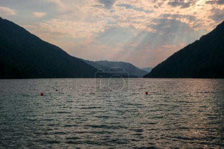 Téléchargez les photos : An early morning at the Weissensee lake in Austria. The sky is bursting with orange. The lake is surrounded by high Alps. Endless chains of mountains. Serenity and peacefulness. Day break - en image libre de droit