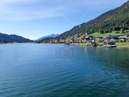 Téléchargez les photos : An idyllic, panoramic view on the Weissensee lake in Austria. The lake is surrounded by high Alps. There is a small village at the lake's shore, with tall church tower. Few clouds. Calmness and peace - en image libre de droit