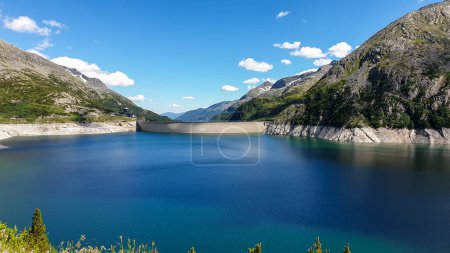 Photo for Dam in Austrian Alps. The artificial lake stretches over a vast territory, shining with navy blue color. The dam is surrounded by high mountains. In the back there is a glacier. Controlling the nature - Royalty Free Image