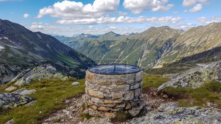 Photo for A pile of stones with a map on top of Arlhoehe in Austrian Alps. The peak is surrounded by high Alps, stretching endlessly. There are a few clouds on the sky. Discovering and experiencing the nature - Royalty Free Image