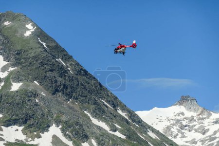Photo for A rescue helicopter flying over the Alpine lake in Austria. Rescue mission. The artificial lake stretches over a vast territory, shining with navy blue color. The dam is surrounded by high mountains - Royalty Free Image