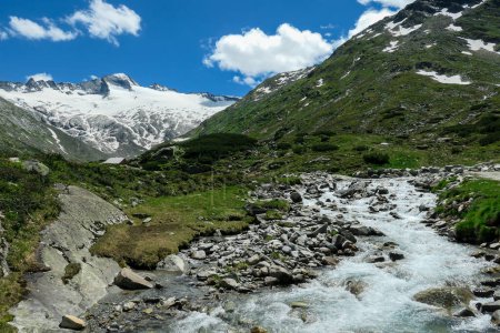 Photo for Panoramic view on huge glacier in Maltal region in Austrian Alps. The valley below it flourishing with green and freshness., small torrent in the middle. Summer in the mountains. Serenity and solitude - Royalty Free Image
