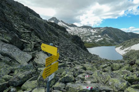 Photo for A sign leading to different destination in Maltal region in Austrian Alps. There is an artificial lake in the back. Summer in the mountains. Serenity and achievement. Choosing the way - Royalty Free Image