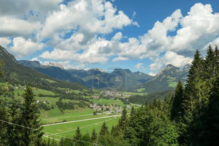 Photo for Panoramic view on a vast Alpine valley. There are sharp mountains and high peaks around. Small town at the bottom. The Alpine slopes are almost barren. Lush green valley. Bright day. Idyllic landscape - Royalty Free Image
