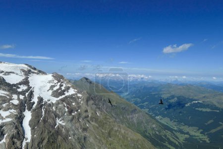 Foto de Vista panorámica desde la cima de Hohe Sonnblick en los Alpes austríacos en Grossglockner. Toda la zona está parcialmente cubierta de nieve, exuberantes prados verdes debajo. Muchas cadenas montañosas en la parte trasera. Día soleado. - Imagen libre de derechos