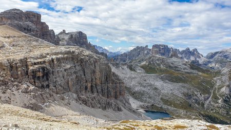 Téléchargez les photos : Vue panoramique sur les Dolomites en Italie. Il y a des pentes abruptes et escarpées autour. Au fond d'une petite vallée, il y a un petit lac bleu marine. Le ciel est plein de nuages mous. Paysage brut - en image libre de droit