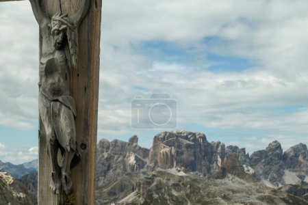 Téléchargez les photos : Une croix en bois avec une figure de Jésus dessus avec vue panoramique sur les Dolomites en Italie. Il y a des pentes abruptes et escarpées autour. Le ciel est plein de nuages mous. Spiritualité et méditation - en image libre de droit