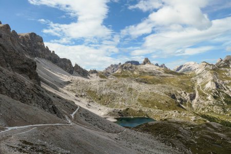 Téléchargez les photos : Vue panoramique sur les Dolomites en Italie. Il y a des pentes abruptes et escarpées autour. Au fond d'une petite vallée, il y a un petit lac bleu marine. Le ciel est plein de nuages mous. Paysage brut - en image libre de droit