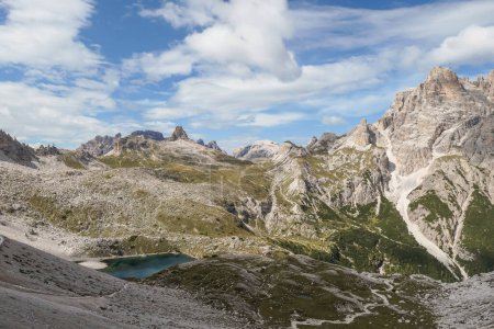 Photo for A panoramic view on Dolomites in Italy. There are sharp and steep mountain slopes around. At the bottom of a small valley there is a small navy blue lake. The sky is full of soft clouds. Raw landscape - Royalty Free Image