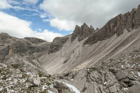 Foto de Vista panorámica de un valle en Dolomitas, Italia. Hay fuertes y empinadas laderas de montaña alrededor. Muchos pierden piedras y guijarros. El cielo está lleno de nubes suaves. Paisaje crudo. Serenidad y calma - Imagen libre de derechos