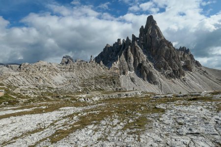 Téléchargez les photos : A capture of high and sharp peaks of Dolomites in Italy. Dried grass on the meadow. The sky is full of soft clouds. Lots of lose stones and pebbles. Raw and desolated landscape. Serenity and calmness - en image libre de droit