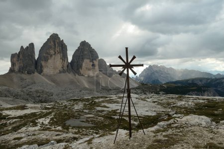 Foto de Una cruz de metal con vistas al famoso Tre Cime di Lavaredo (Drei Zinnen) en Dolomitas italianas. Las montañas están rodeadas de densas nubes. Espiritualidad y logro. Maravilla natural. - Imagen libre de derechos