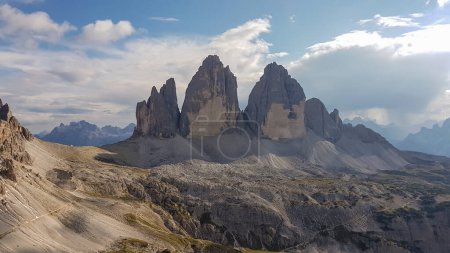 Photo for The famous Tre Cime di Lavaredo (Drei Zinnen) and surrounding mountains in Italian Dolomites. The mountains are surrounded by thick clouds. Stony valley below. Few narrow pathways on the side. Freedom - Royalty Free Image