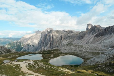 Foto de Pequeños lagos de color azul marino en el fondo del valle de los Alpes italianos. Los lagos están rodeados de picos altos y empinados. Las laderas son de un verde exuberante. El cielo está lleno de nubes suaves. Paisaje crudo. Remedio - Imagen libre de derechos