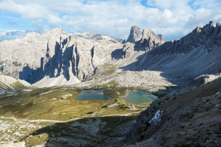 Foto de Pequeños lagos de color azul marino en el fondo del valle de los Alpes italianos. Los lagos están rodeados de picos altos y empinados. Las laderas son de un verde exuberante. El cielo está lleno de nubes suaves. Paisaje crudo. Remedio - Imagen libre de derechos