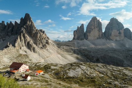 Foto de Drei Zinnenhuette and a small chapel, with red rooftop and small bell tower with the view on the Tre Cime (Drei Zinnen) in Italian Dolomites. There are high Alpine peaks around. Sunny day. Shelter - Imagen libre de derechos