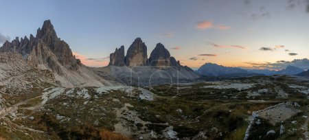 Foto de Una captura panorámica de la puesta de sol sobre Tre Cime di Lavaredo (Drei Zinnen) y las montañas circundantes en los Dolomitas italianos. Las montañas están rodeadas de nubes rosas y anaranjadas. Hora dorada. Serenidad - Imagen libre de derechos