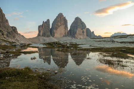 Photo for Golden hour over the Tre Cime di Lavaredo (Drei Zinnen), mountains in Italian Dolomites. The peaks reflect in a paddle. The mountains are surrounded with orange and pink clouds. Sunset time. Serenity - Royalty Free Image