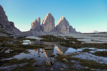 Photo for A panoramic view on the Tre Cime di Lavaredo (Drei Zinnen), mountains in Italian Dolomites. The mountains are reflecting in small paddle. Desolated and raw landscape. Early morning. Daybreak - Royalty Free Image