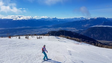 Foto de A woman snowboarding down the slope of Gerliten in Austria. There are endless snow capped mountain chains. Few tress in the middle of white slopes. Winter ski resort. Skiing remedy. - Imagen libre de derechos