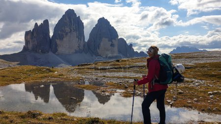 Téléchargez les photos : A woman in hiking outfit enjoying the view on the famous Tre Cime di Lavaredo (Drei Zinnen), mountains in Italian Dolomites. The mountains are reflecting in small paddle. Desolated and raw landscape. - en image libre de droit