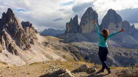 Foto de Una mujer en traje de senderismo de pie con los brazos abiertos y disfrutando de la vista sobre el famoso Tre Cime di Lavaredo (Drei Zinnen), montañas en los Dolomitas italianos. Paisaje desolado y crudo. Libertad - Imagen libre de derechos