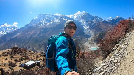 Photo for A man hiking and taking a selfie with snow caped Annapurna chain in the back, Annapurna Circuit Trek, Himalayas, Nepal. High mountains around. The man is admiring the landscape. Serenity and calmness. - Royalty Free Image