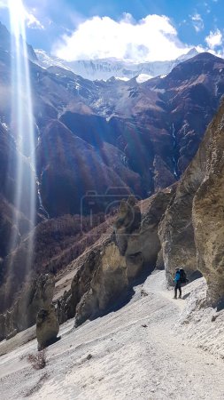 Téléchargez les photos : Un homme traversant un passage dangereux le long de la zone de glissement de terrain sur le chemin du camp de base de Tilicho, Annapurna Circus, Himalaya, Népal. Paysage sec et désolé. Pentes raides et abruptes. Randonnée extrême - en image libre de droit