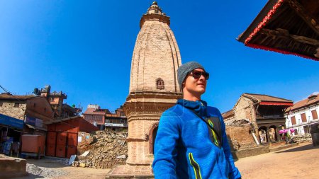 Foto de Un hombre en un gorro tomando una selfie con una Stupa en la plaza principal de Bhaktapur, Nepal. Está disfrutando descubriendo un nuevo lugar. La Stupa es el punto central de la plaza. Lista del patrimonio UNESCO. - Imagen libre de derechos