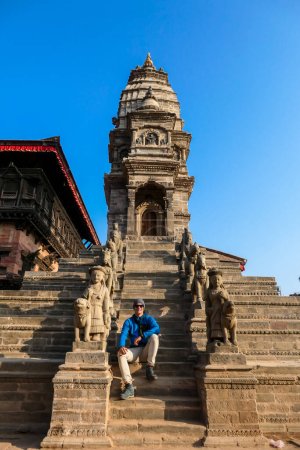 Ein Mann sitzt an der Treppe zu einem der Tempel in Bhaktapur, Nepal. Auf beiden Seiten der Treppe befinden sich hinduistische Götter, die den Eingang zum Tempel bewachen. Die Wächter sind wirklich groß.