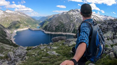 Photo for Man with hiking backpack taking a selfie above an artificial lake at a dam in Austria. The lake has navy blue color. High Alps around. There is a glacier in the back. Adventure and discovery - Royalty Free Image