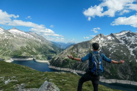 Photo for Man with hiking backpack admiring a view on an artificial lake at a dam in Austria from above. The lake has navy blue color. High Alps around. There is a glacier in the back. Adventure and discovery - Royalty Free Image