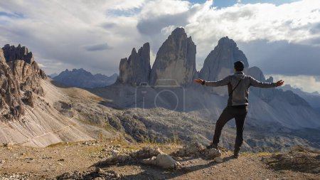 Foto de Un hombre en traje de senderismo de pie con los brazos abiertos y disfrutando de la vista sobre el famoso Tre Cime di Lavaredo (Drei Zinnen), montañas en los Dolomitas italianos. Paisaje desolado y crudo. Libertad - Imagen libre de derechos