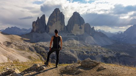 Téléchargez les photos : A man in hiking outfit standing on top of Sextner Stein and enjoying the view on the famous Tre Cime di Lavaredo (Drei Zinnen), mountains in Italian Dolomites. Desolated and raw landscape. Freedom - en image libre de droit