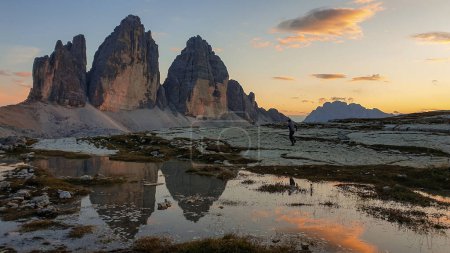 Téléchargez les photos : A man enjoying the sunset over the Tre Cime di Lavaredo (Drei Zinnen) mountains in Italian Dolomites. The peaks reflect in a paddle. The mountains are surrounded with orange and pink clouds. Freedom - en image libre de droit