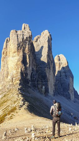 Foto de Un hombre con una gran mochila de senderismo disfrutando de la vista de cerca del Tre Cime di Lavaredo (Drei Zinnen), montañas en los Dolomitas italianos. Muro de montaña afilado y alto. Paisaje desolado y crudo. Remedio - Imagen libre de derechos