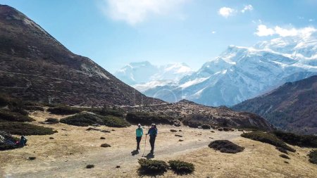 Téléchargez les photos : A couple trekking in the Manang Valley, Annapurna Circus Trek, Himalayas, Nepal, with the view on Annapurna Chain and Gangapurna. Dry and desolated landscape.  High snow capped mountain peaks. Freedom - en image libre de droit