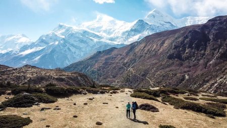 Téléchargez les photos : Un couple trekking dans la vallée de Manang, Annapurna Circus Trek, Himalaya, Népal, avec vue sur la chaîne de l'Annapurna et Gangapurna. Paysage sec et désolé. Hauts sommets enneigés des montagnes. Liberté - en image libre de droit