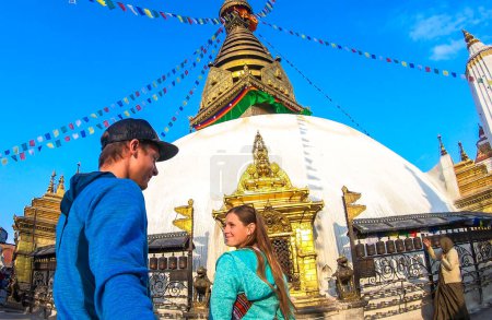 Foto de Couple walking into the boudhanath Temple in Kathmandu, Nepal. Many colourful prayer flags with 'om mani padme hum' mantra written on them above. The round temple is painted white.Golden decoration - Imagen libre de derechos