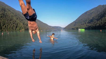 Téléchargez les photos : A couple playing at the Weissensee lake in Austrian Alps. The man is jumping into the water from the wooden pier. The woman is splashing the water around. Happiness and relaxation - en image libre de droit