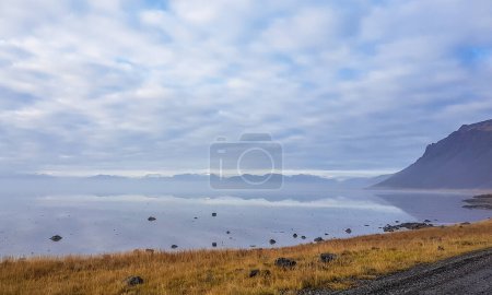 Foto de A misty view on the fjords. Cumulus clouds spreads on the sky. Grass on the shore is dry. A little piece of a road in the corner. Mystical and magical landscape, gull of natural wonders. - Imagen libre de derechos