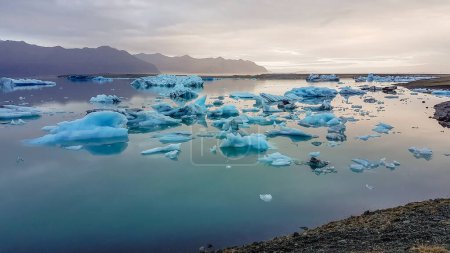 Téléchargez les photos : Wast and cold glacier lagoon, with the glacier cap in the back. Huge and massive ice bergs are slowly drifting towards the sea. Global warming causing the glacier's melting. Pebbles on the shore - en image libre de droit