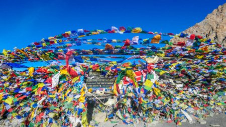 Photo for The waving flags at the top of Thorung La Pass, Annapurna Circuit Trek, Nepal. Congratulations for the effort. Colorful Prayer flags attached to the stone wall, blow by the wind. Clear sky. - Royalty Free Image
