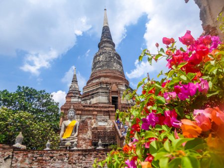 Téléchargez les photos : Un magnifique temple d'Ayutthaya, Thaïlande. Au premier plan sont les fleurs colorées, et le temple avec une grande statue de Bouddha est en arrière-plan. Temple construit en brique rouge. contraste rouge, bleu et vert. - en image libre de droit