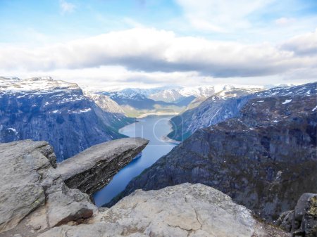 Foto de Famous rock formation, Trolltunga with a view from the above on Ringedalsvatnet lake, Norway. Rock hanging. Slopes of the mountains are partially covered with snow. The water of the lake is navy blue. - Imagen libre de derechos